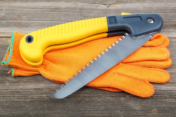 Folding garden saw with work gloves on wooden boards.