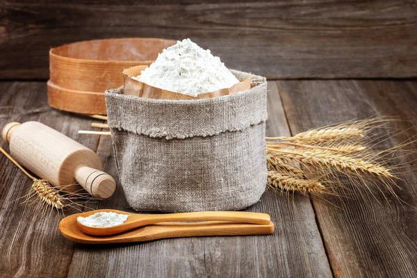 Flour in a canvas bag, wheat ears on a wooden background.