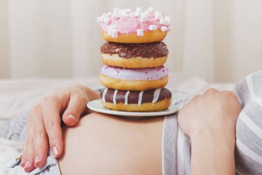 Göbek, yumuşak odak arka plan üzerinde farklı renkli donut ile hamile kadın