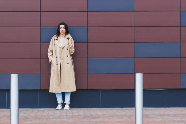 Bej bir palto ve kot sokak, yumuşak odak arka plan üzerinde güzel kadın