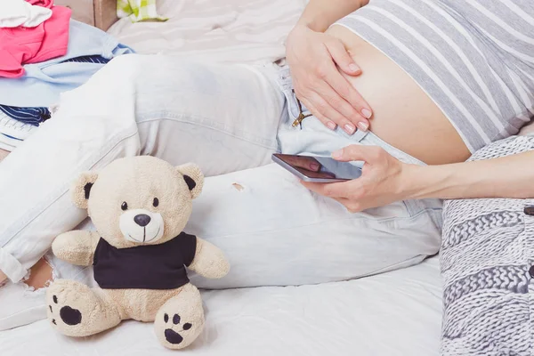 Pregnant woman with a teddy bear and various clothes for a newborn, top view