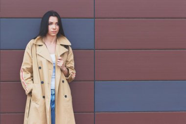 Bej bir palto ve kot sokak, yumuşak odak arka plan üzerinde güzel kadın