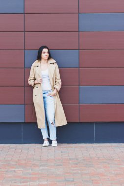 Bej bir palto ve kot sokak, yumuşak odak arka plan üzerinde güzel kadın