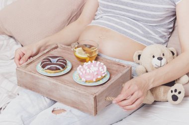 Farklı renkli çörek ve çay, yumuşak odak arka plan ile hamile kadın