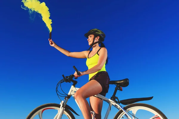 Young woman on the top of the mountain holds a yellow signal smoke in her hand