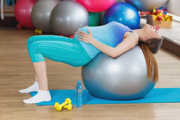 妊娠中の女性がジム ソフト フォーカスの背景のマットの上に座っています — ストック写真