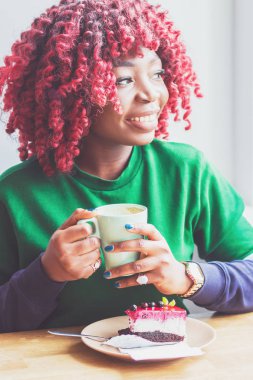 Kahve veya çay keyfi sıcak içecek fincan tutarak rahat kıyafetler giymiş genç esmer kadın. Sabah kafede harcama siyah öğrenci kız