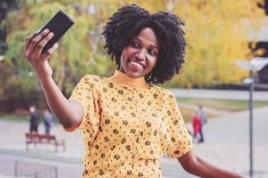 Genç gülümseyen rahat kıyafetler giymiş esmer kadın onun telefonu, arka plan bulanık bir fotoğraf yapmak