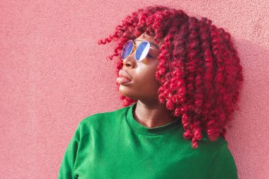 Sevimli genç Afrikalı kadın mavi güneş gözlüğü. Moda ve şık bir kız pembe duvara yakın, yumuşak odak arka plan poz