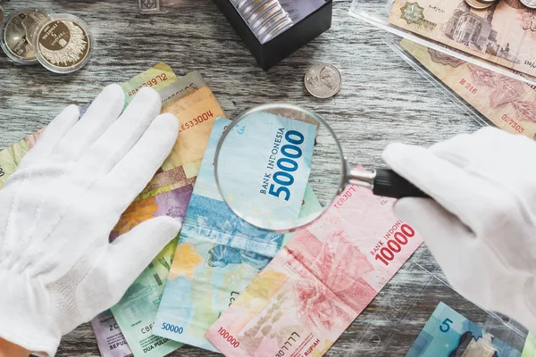 Manos en guantes blancos, diferentes dólares americanos y rupias indonesias, concepto numismático — Foto de Stock