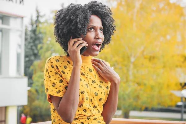 Young smiling dark-skinned woman dressed in casual clothes talking to her phone