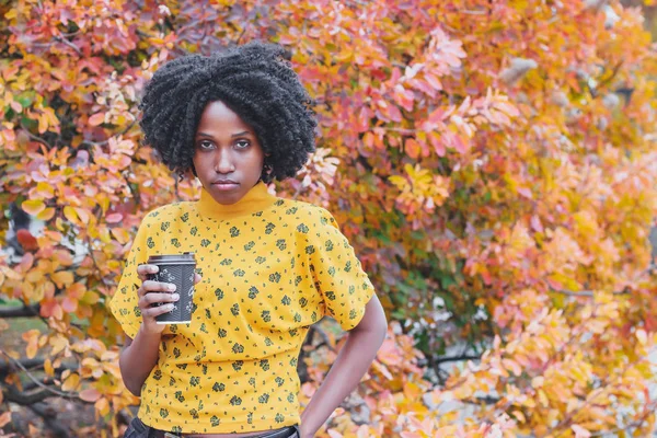 Young dark-skinned woman dressed in casual clothes holding cup of hot drink