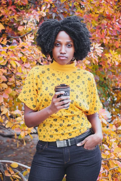Young dark-skinned woman dressed in casual clothes holding cup of hot drink