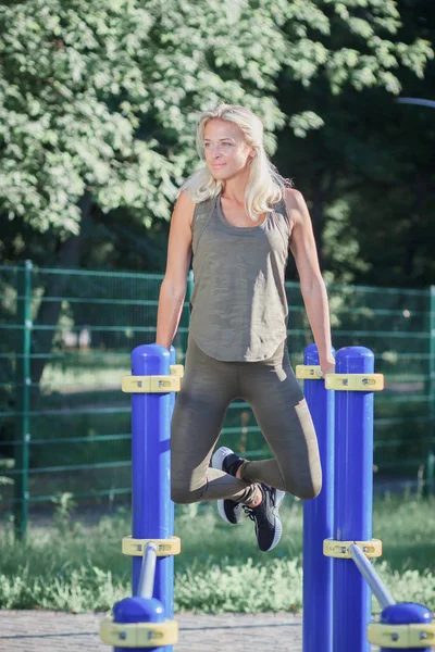 Mooie vrouw in Sneakers en sportkleding maakt sportoefeningen op het atletische veld, onscherpe achtergrond — Stockfoto