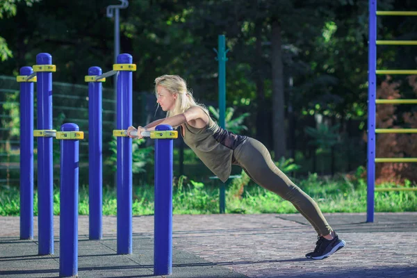 Mooie jonge vrouw maakt sportoefeningen op het sportterrein, onscherpe achtergrond — Stockfoto