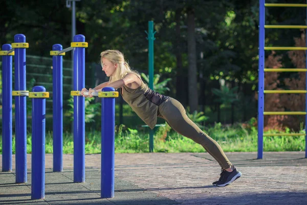 Mooie jonge vrouw maakt sportoefeningen op het sportterrein, onscherpe achtergrond — Stockfoto