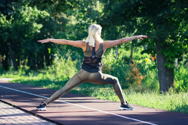 Mooie jonge vrouw maakt sportoefeningen op het sportterrein, onscherpe achtergrond — Stockfoto