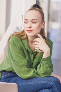 Genç ve güzel bir kadın elinde akıllı bir telefonla oturuyor, yumuşak odaklı bir geçmişi var.