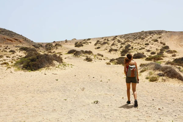 Lost in the desert. Young female hiker walking between desert dunes with uncertain step in Lanzarote, Canary Islands.