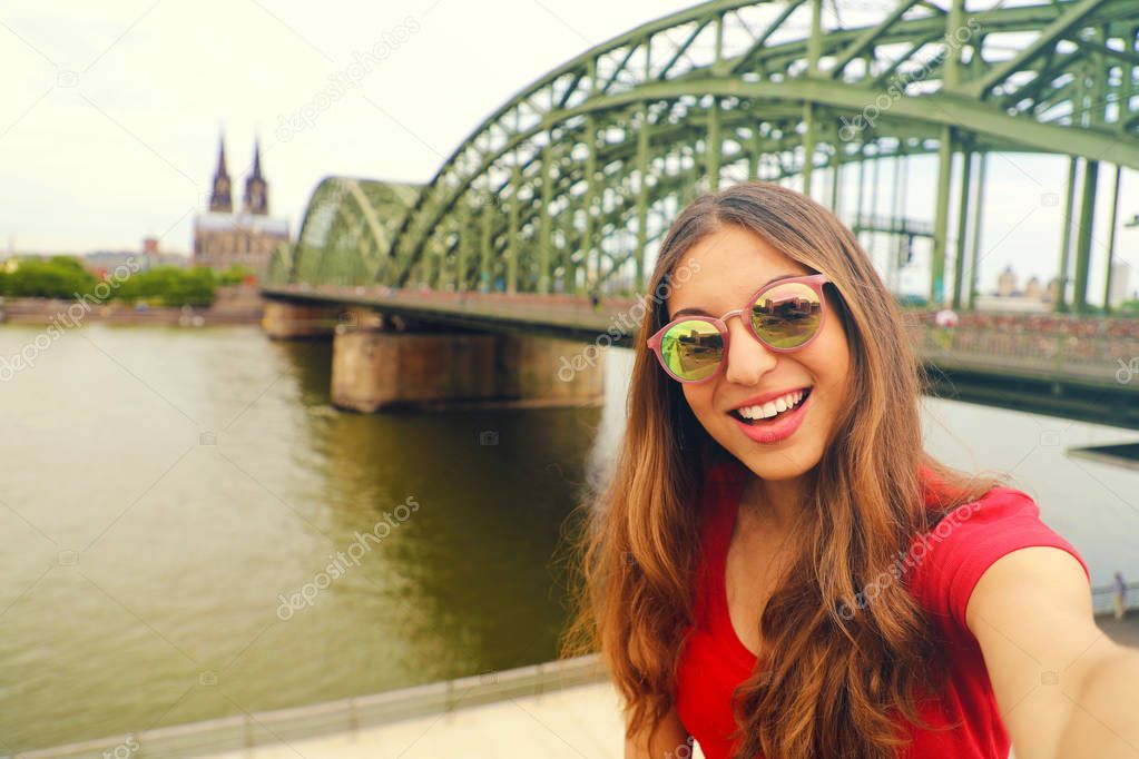 Selfie photo of young fashion woman in Cologne with Hohenzollern Bridge and Cathedral on the background, Cologne, Germany. Traveling in Europe. Vintage Filter.