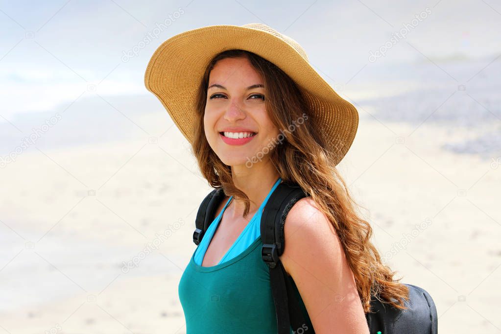 Adventure girl with backpack and straw hat looking to the camera. Young woman exploring Canarian Coast with sand dunes of Lanzarote, Spain.