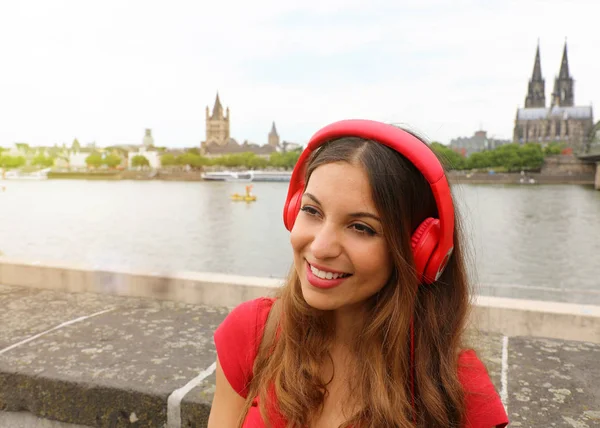 Smilling headset woman listening to music with european landscape on the background. Portrait of pretty girl with famous cathedral of Cologne, Germany. Concept urban, technology and youth.