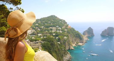 Güzel genç kadın modeli ile hasır şapka Capri adasında Faraglioni deniz yığını ve mavi kristal su ile arka planda, Capri, İtalya. Afiş panorama.