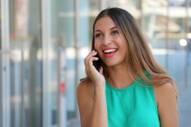 Cam duvar telefonla konuşurken alışveriş merkezinin yakınında duran neşeli genç bayan. Pretty genç kız ile akıllı telefon açık çağrı.