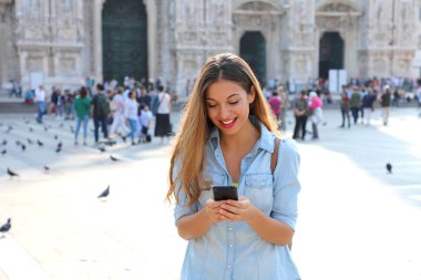 Güneşli bir günde meydanda akıllı telefon ayakta üzerinde gömlek manifatura giyen kadın