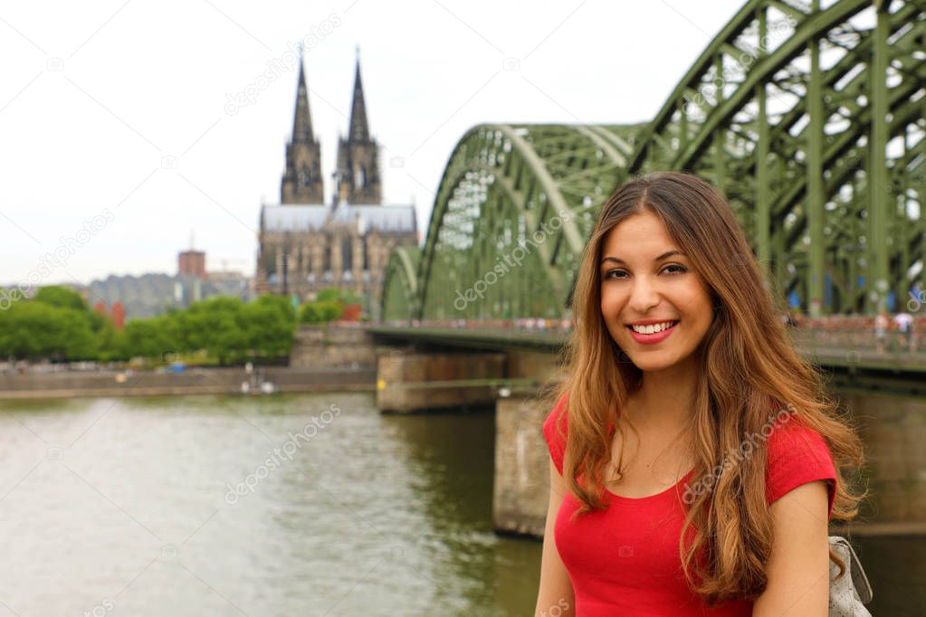 Europe tourist traveler woman. Happy smiling girl enjoying travel in Germany. Beautiful traveler girl posing in front of the camera with Cologne Cathedral and Hohenzollern Bridge on the Rhine River.