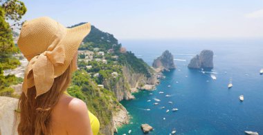 Güzel genç kadın modeli Capri adasında Faraglioni deniz yığını ve mavi deniz suyu arka planda, Capri, İtalya ile hasır şapka ile