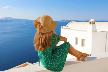 Duvarda oturan ve Santorini, Yunanistan güzel manzara isteyen genç kadın. Arkadan Görünüş.