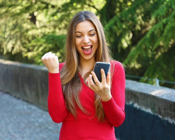 Mujer eufórica mirando su teléfono inteligente al aire libre —  Fotos de Stock