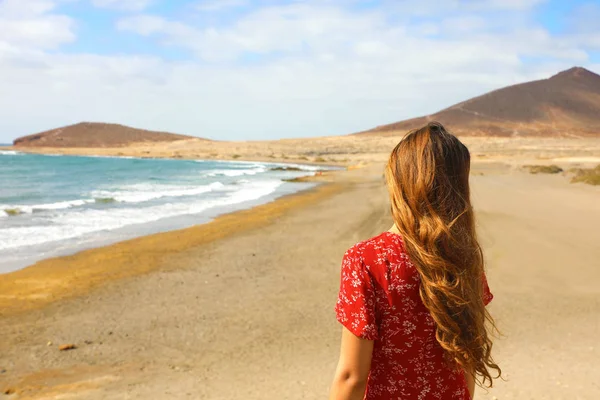 Tillbaka syn på vacker flicka i röd klänning stående på stranden, El Medano, Teneriffa — Stockfoto