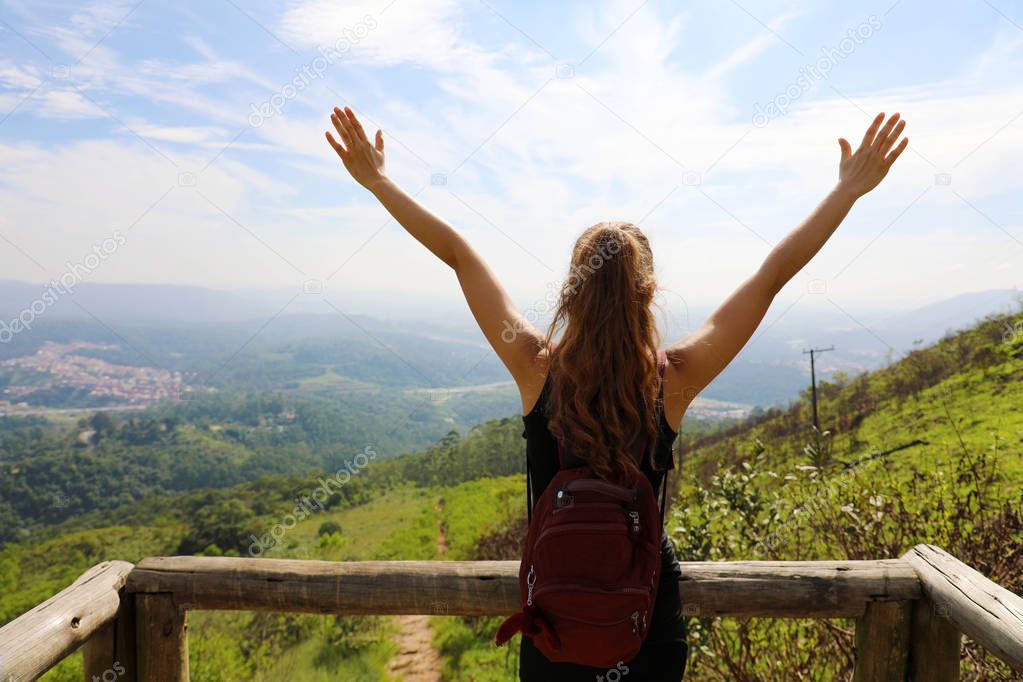 Hiker woman standing with hands up achieving the top. Girl welcomes a sun. Successful woman hiker open arms on mountain top. Girl enjoying nature on Jaragua Peak, Sao Paulo, Brazil.