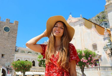 İtalya'da yaz tatili. Arka planda Taormina köyü ile hasır şapka ve kırmızı elbiseli genç kadının portresi, Sicilya, İtalya.