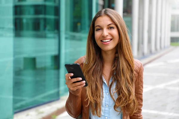 Joven mujer de negocios hermosa sonriendo y mirando a la cámara mientras sostiene el teléfono móvil en su mano. Concepto empresarial . — Foto de Stock