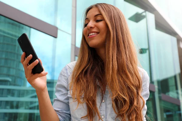 스마트 폰을 사용하여 비즈니스 지구에서 걷는 행복한 미소 여성. 낮은 각도. — 스톡 사진