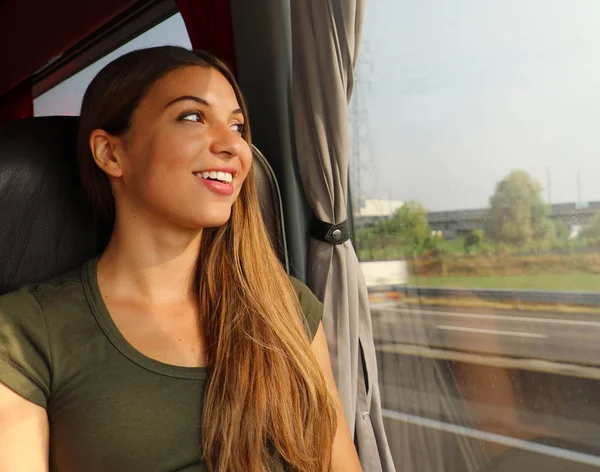 Mladá krásná žena, která se dívá skrz okno autobusu. Šťastný cestující autobusem, sedící v křesle a procházející oknem. — Stock fotografie