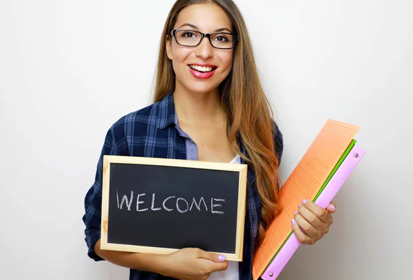 Young female teacher holding folders and blackboard with written welcome. — Stock Photo, Image