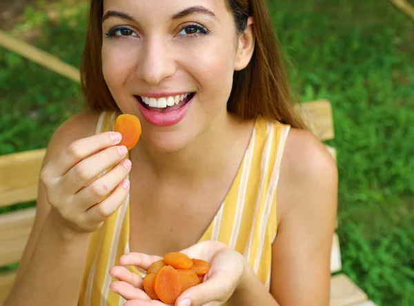 Gyönyörű fiatal nő eszik szárított gyümölcsök a parkban. Egészséges táplálkozás koncepció. — Stock Fotó