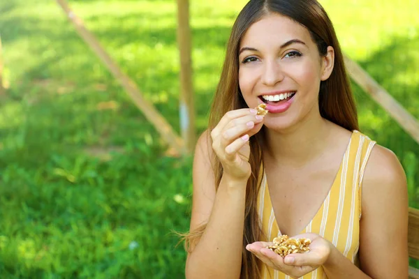 Mulher sorridente bonita comendo nozes no parque. Conceito de alimentação saudável . — Fotografia de Stock