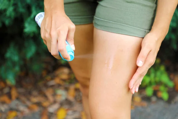 Donna spruzzando insetto repellente sulla gamba all'aperto in natura utilizzando bottiglia spray. Zanzara repellente. Spray per insetti anti insetti . — Foto Stock