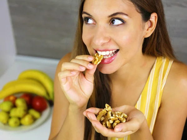 Красивая молодая женщина улыбается и ест грецкие орехи дома. Закрыться сверху, глядя в сторону . — стоковое фото