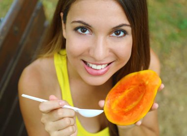 Parkta sağlıklı papaya yiyen kız kameraya bakıyor. Kadın açık tropikal taze meyve yeme.
