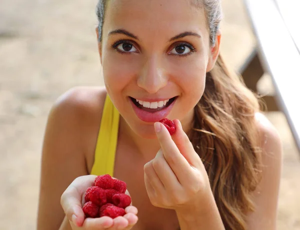 Uma jovem saudável a comer framboesas no parque. Menina feliz ter café da manhã saudável ao ar livre . — Fotografia de Stock