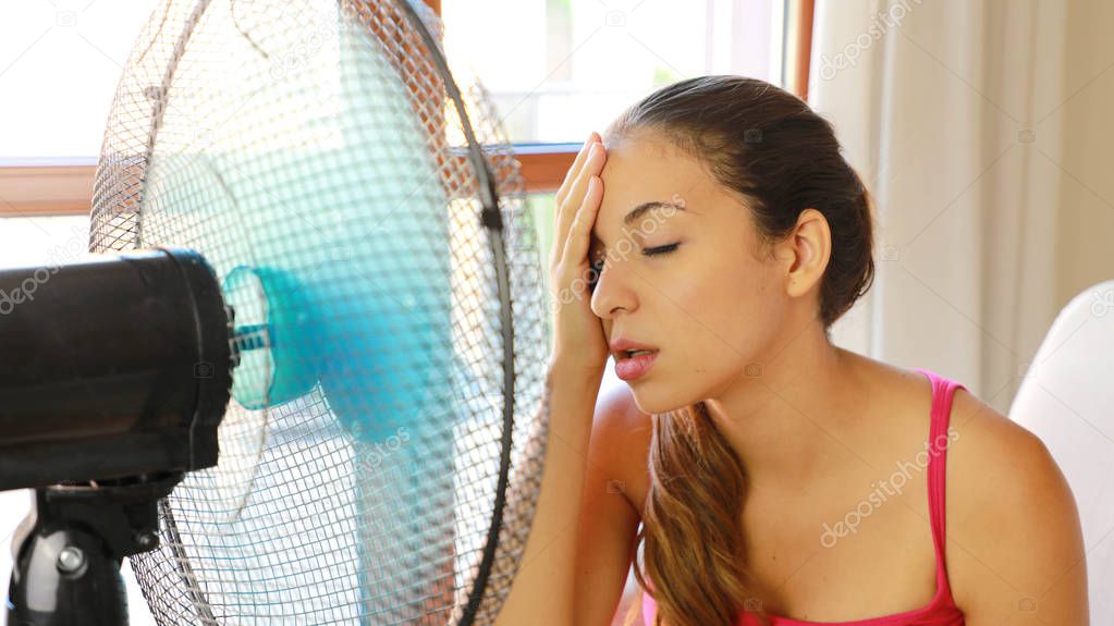 Young woman at home in hot summer day in front of the working fan suffering from summer heat.