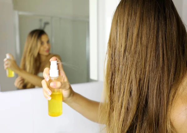 Молода жінка наносить масляну маску на кінчики волосся перед дзеркалом. Концепція догляду за волоссям. Фокус на волоссі . — стокове фото