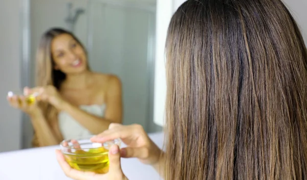 Усміхнена дівчина наносить масляну маску на волосся перед дзеркалом. Концепція догляду за волоссям. Фокус на волоссі . — стокове фото