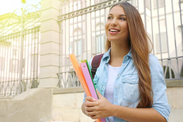 Menina estudante alegre feliz segurando pastas ao ar livre olhando para o lado o espaço de cópia . — Fotografia de Stock